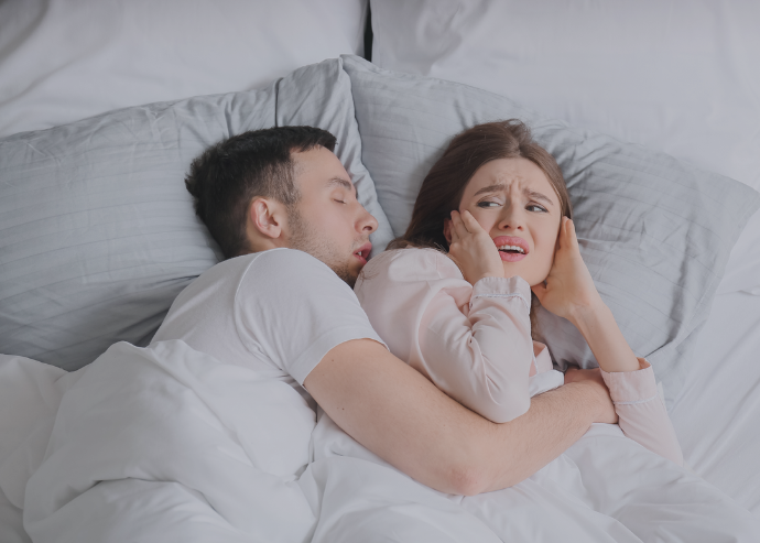 Eine Frau liegt im Bett und zeigt sich gestört von ihrem schnarchenden Partner, ein häufiges Problem, das in der HNO-Praxis adressiert wird.