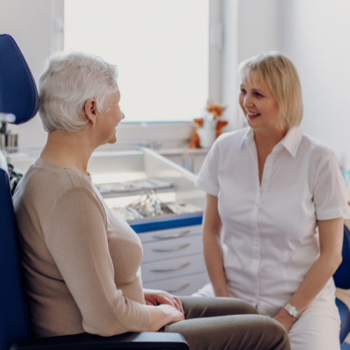 Ein modernes Wartezimmer mit grauen Stühlen und einer orangefarbenen Wand. Ein älterer Mann liest eine Zeitschrift, was die ruhige und komfortable Warteumgebung hervorhebt.igt das persönliche und patientenorientierte Vorgehen der Ärztin, was Vertrauen und Fürsorge betont.