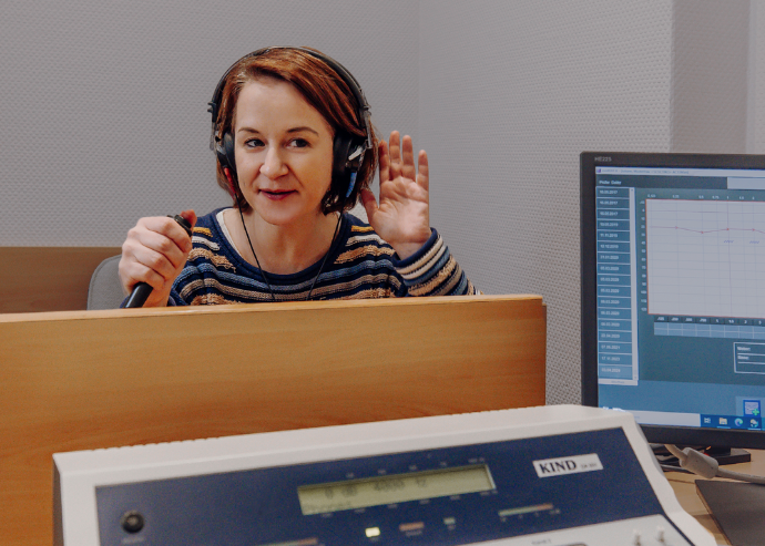 Eine Frau mittleren Alters nimmt an einem Hörtest teil, bei dem sie Kopfhörer trägt und auf Töne reagiert, die über einen Computer gesteuert werden.