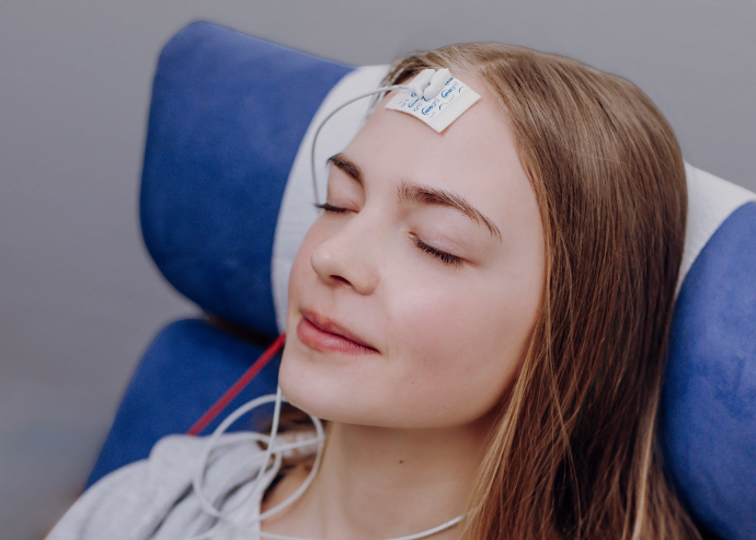 Ein junges Mädchen entspannt sich während einer EEG-Untersuchung im Schlaflabor, mit Sensoren auf der Stirn, die ihre Gehirnaktivität überwachen